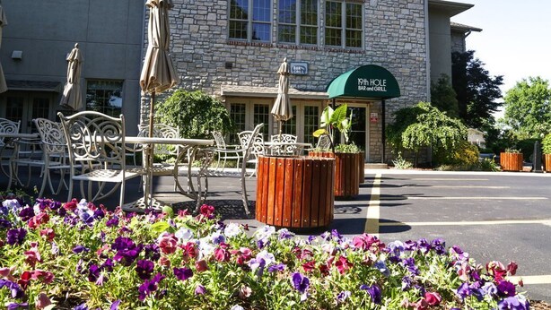 A building with a stone facade, outdoor seating with umbrellas, and a sign for '19th Hole Bar and Grill'.