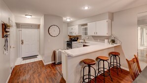 A modern kitchen with white cabinetry, a central island with stools, a built-in oven, and a microwave.