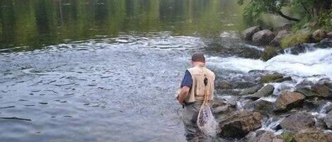 A person standing by a river with a backpack, surrounded by rocks and greenery.