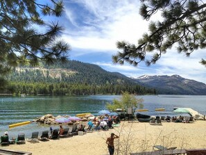 Une plage au bord d’un lac, avec des bateaux, des chaises et une personne qui se promène.
