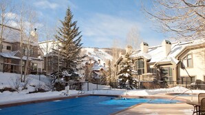 A swimming pool area with snow-covered surroundings and buildings in the background.