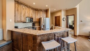 A kitchen with wooden cabinets, a granite countertop, a stainless steel refrigerator, and a microwave.