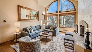 A spacious living room with a large arched window, a fireplace, and a cozy seating area with a blue sofa and a round coffee table.