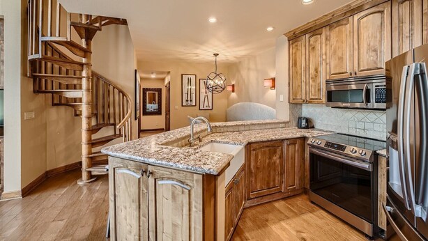 A kitchen with wooden cabinets, a granite countertop, a built-in oven, and a stainless steel refrigerator.