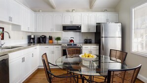 Una cucina moderna con mobili bianchi, elettrodomestici in acciaio inossidabile, un tavolo da pranzo in vetro e sedie in vimini.