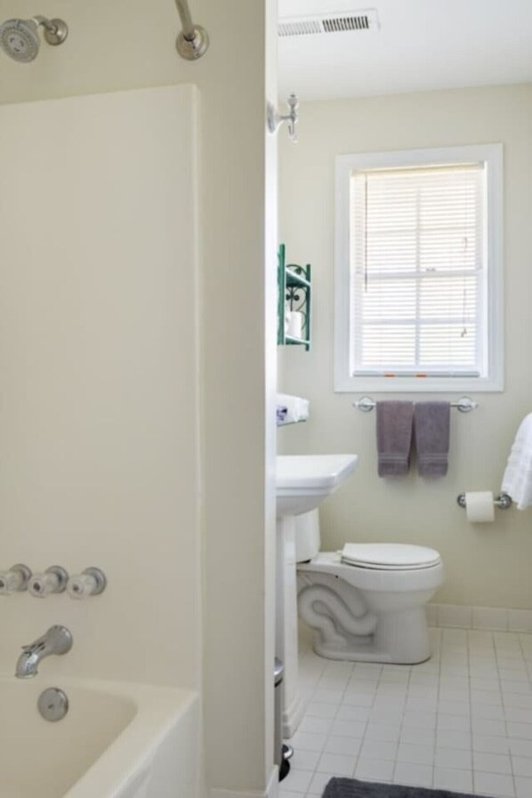 A bathroom with a bathtub, toilet, sink, and a window with blinds.