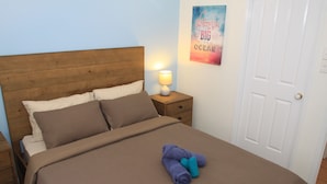 Una cama bien hecha con una colcha marrón y dos almohadas, una lámpara de noche y un cartel en la pared.