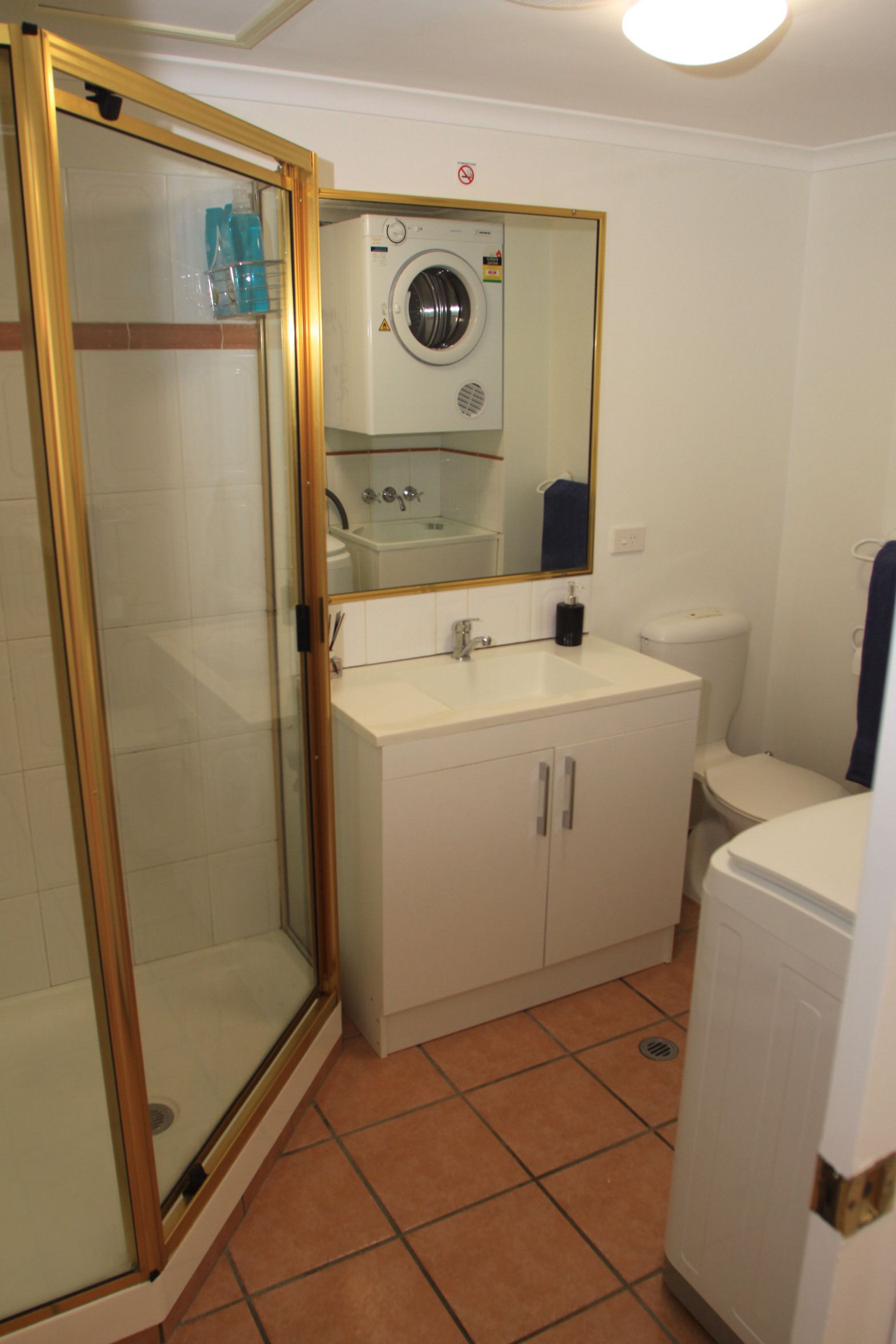 A bathroom with a glass-enclosed shower, a washing machine, a sink, and a toilet.