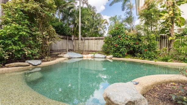 Piscina cristalina rodeada de vegetación tropical y una valla de madera.