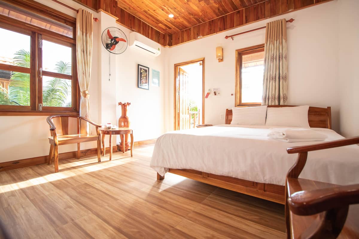 A wooden-floored bedroom with a bed, a chair, a small table, and a window with curtains.
