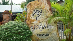 Un letrero de piedra con un símbolo de casa y el texto "Yonghia Bungalow" rodeado de follaje.