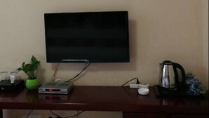 A room with a flat-screen TV mounted on the wall, a small table with a plant, a kettle, and a few other items. - Yan Yu Qing Cheng Inn (Chengdu)