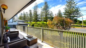 A balcony with wicker furniture, a glass-top table, and a view of trees and a road.