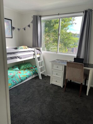 Cozy bedroom with a bunk bed, desk, and dresser, offering a view of lush greenery outside.