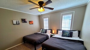 A bedroom with two single beds, a ceiling fan, and two windows with blinds.