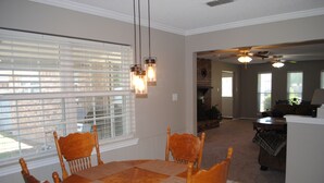 A dining area with a wooden table and chairs, a window with blinds, and a ceiling fan.