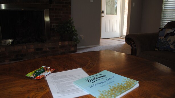 A wooden table with a welcome card, a snack packet, and papers.