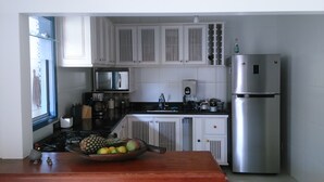 Una cocina compacta con armarios blancos, un refrigerador de acero inoxidable y una mesa de madera con un frutero.