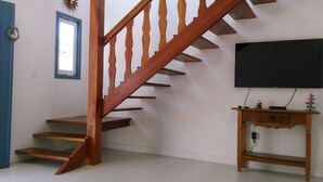 Una escalera con barandillas de madera, un televisor de pantalla plana montado en la pared y una pequeña consola de madera con algunos objetos encima.