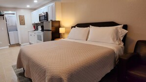 Een slaapkamer met een bed, nachtkastje, lamp en stoel.