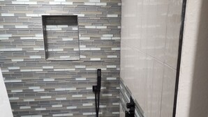 Een douchegedeelte met een betegelde wand en een douchekop.
