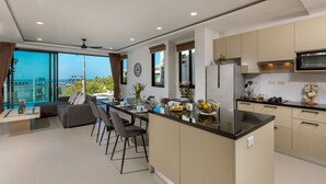 Een moderne keuken met een centraal eiland, een eetgedeelte met een bank en stoelen, en grote ramen met uitzicht op de zee.
