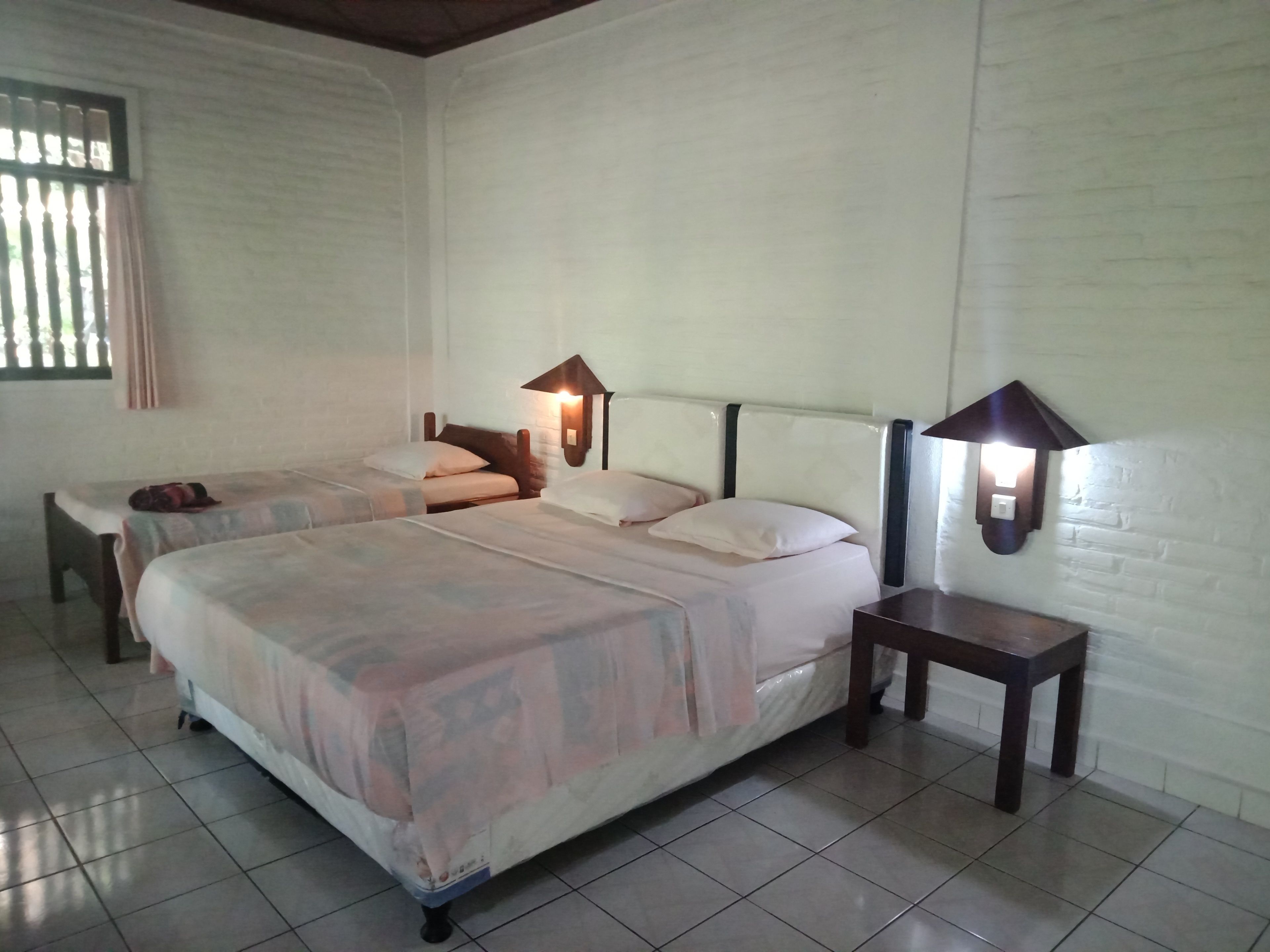 A room with two beds, a small table, and a wall-mounted lamp.