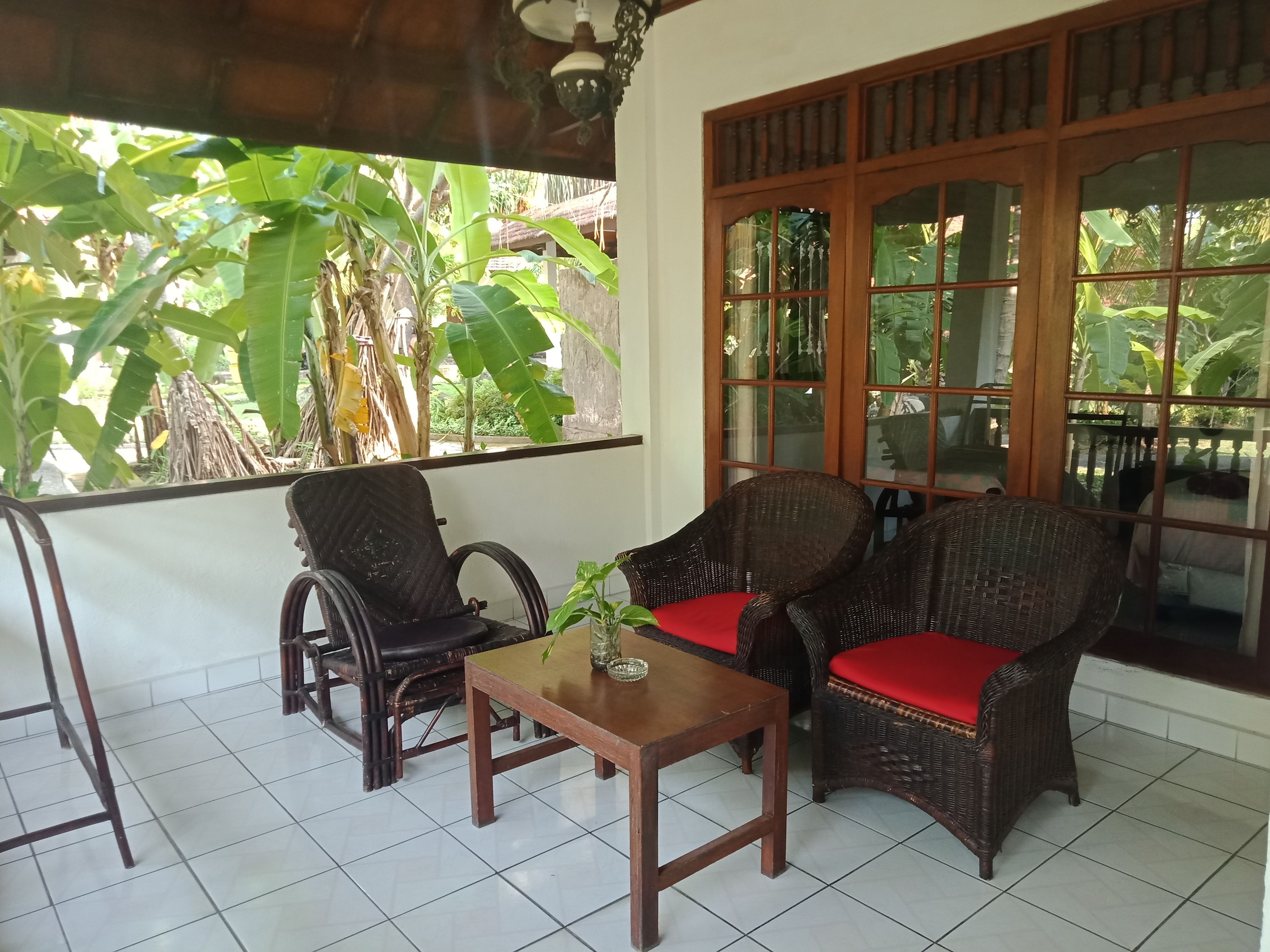 A room with wicker furniture, a tiled floor, and a large window with a view of greenery.
