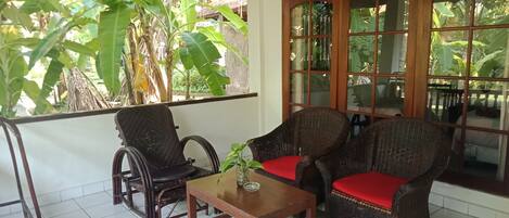 A room with wicker furniture, a tiled floor, and a large window with a view of greenery.