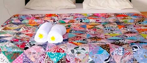 Una cama con un colcha colorida, dos almohadas y una lámpara fijada a la pared.