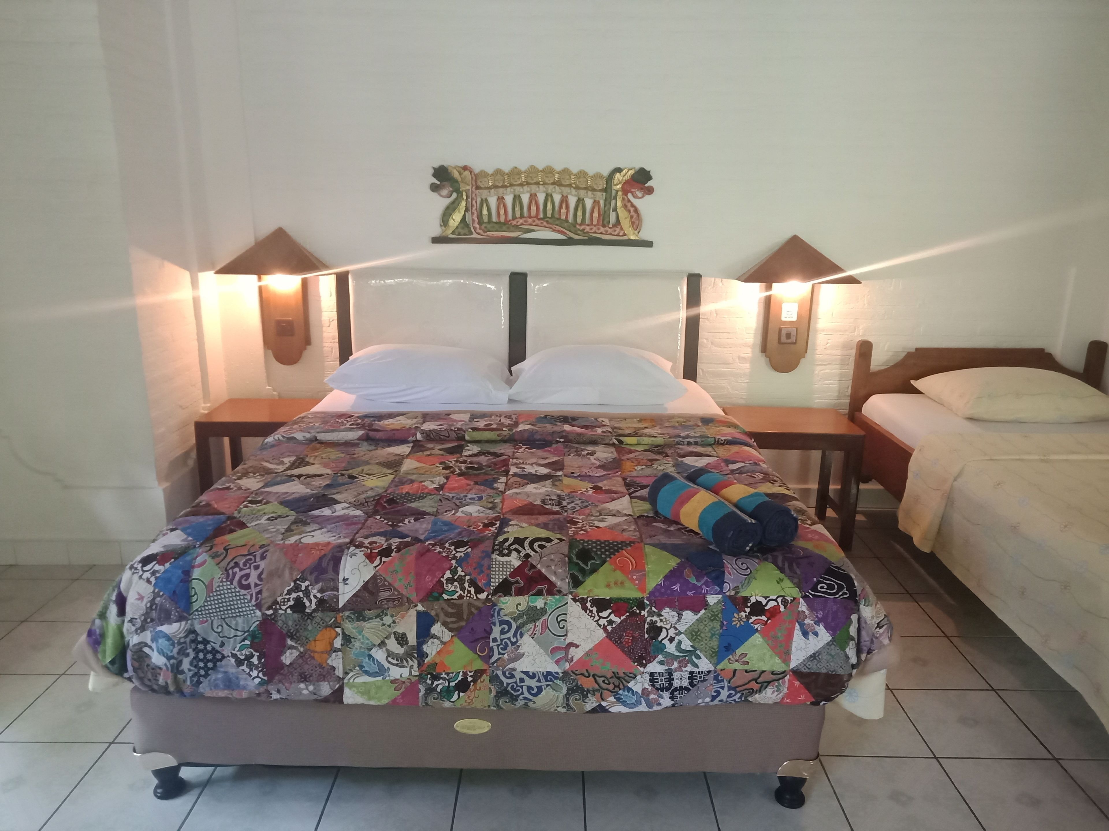 A bed with a colorful quilt, two bedside tables with lamps, and a decorative wall piece above the bed.