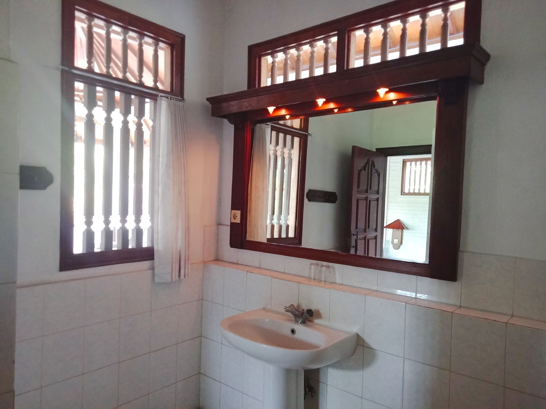 A bathroom with a white sink, a mirror with a wooden frame, and a window with vertical bars.