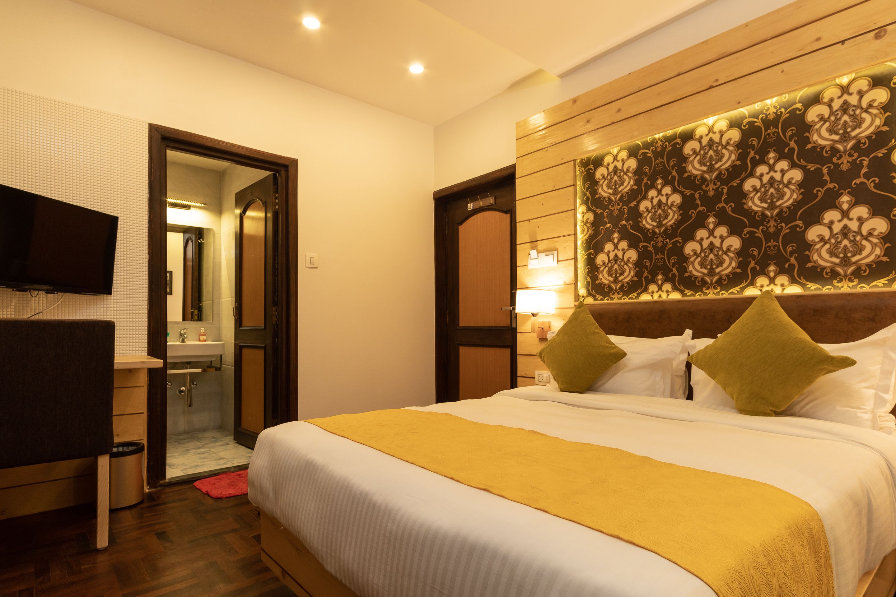 Ein Hotelzimmer mit Bett, Wandfernseher, Badezimmer mit Spiegel und einem Holzkopfteil mit Musterdesign.