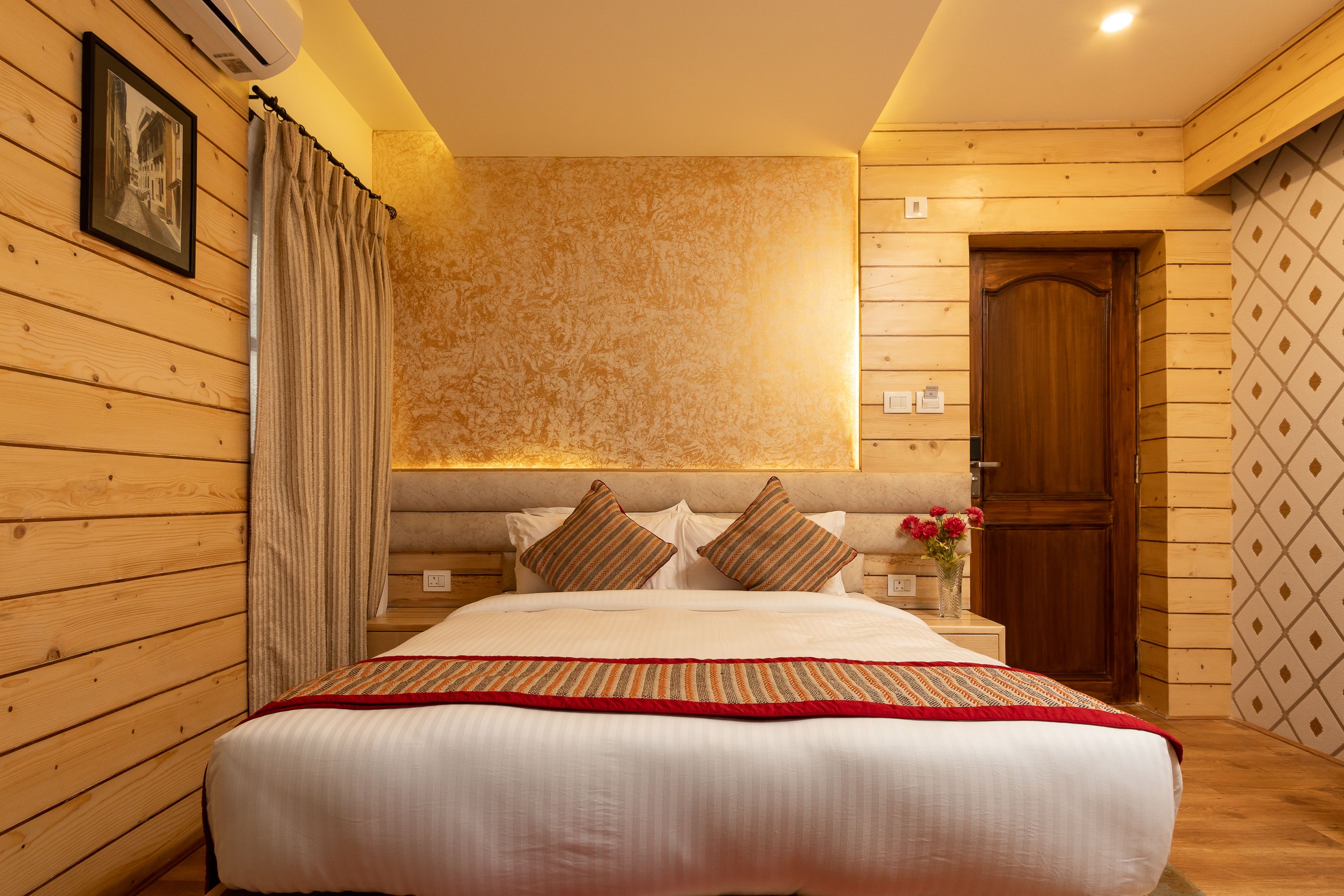 Una cama bien hecha con un edredón a rayas, paredes de madera y una puerta de madera.