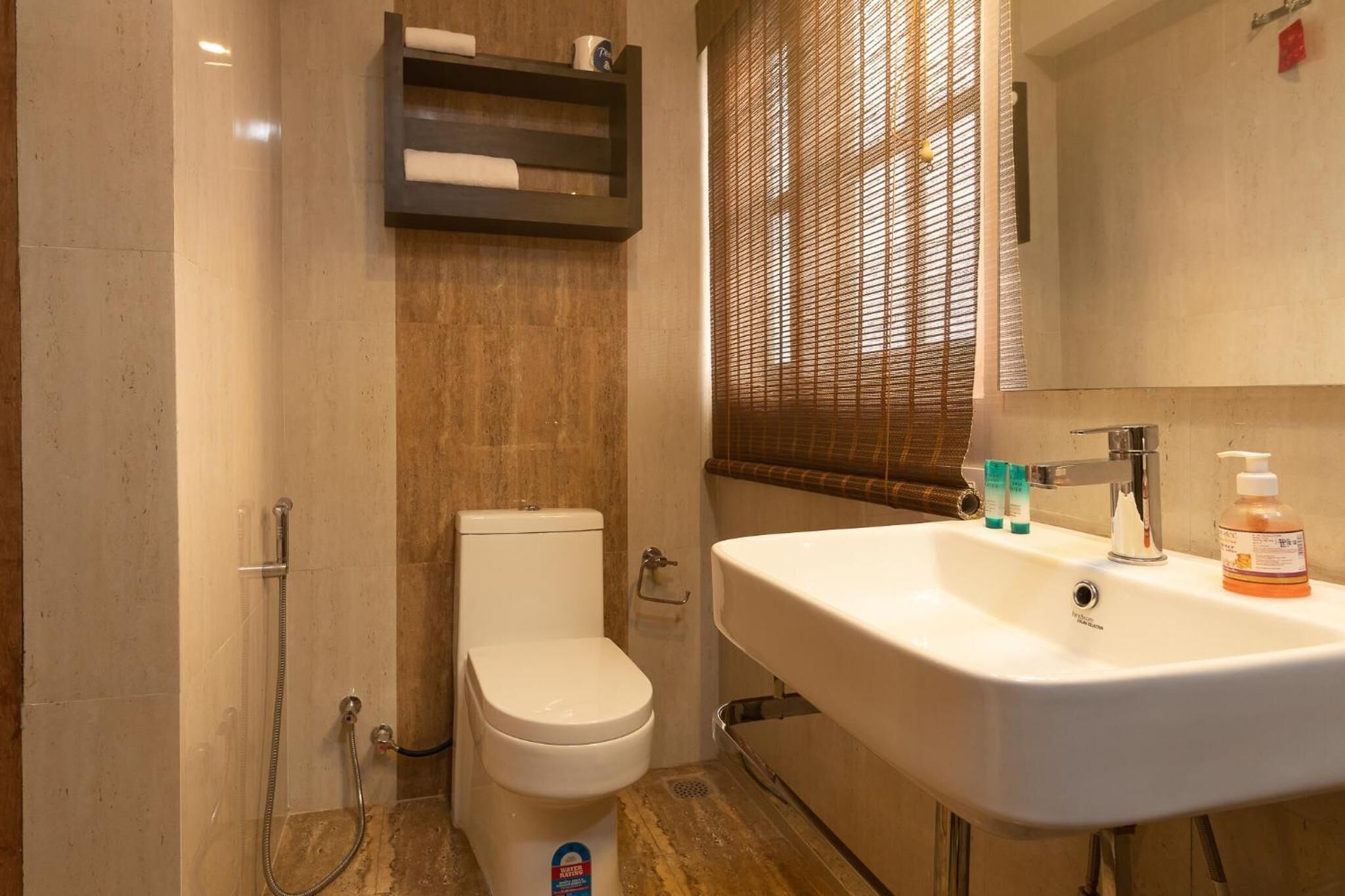 Une salle de bain équipée de toilettes, d’une douche, d’un lavabo et d’une fenêtre avec des stores.