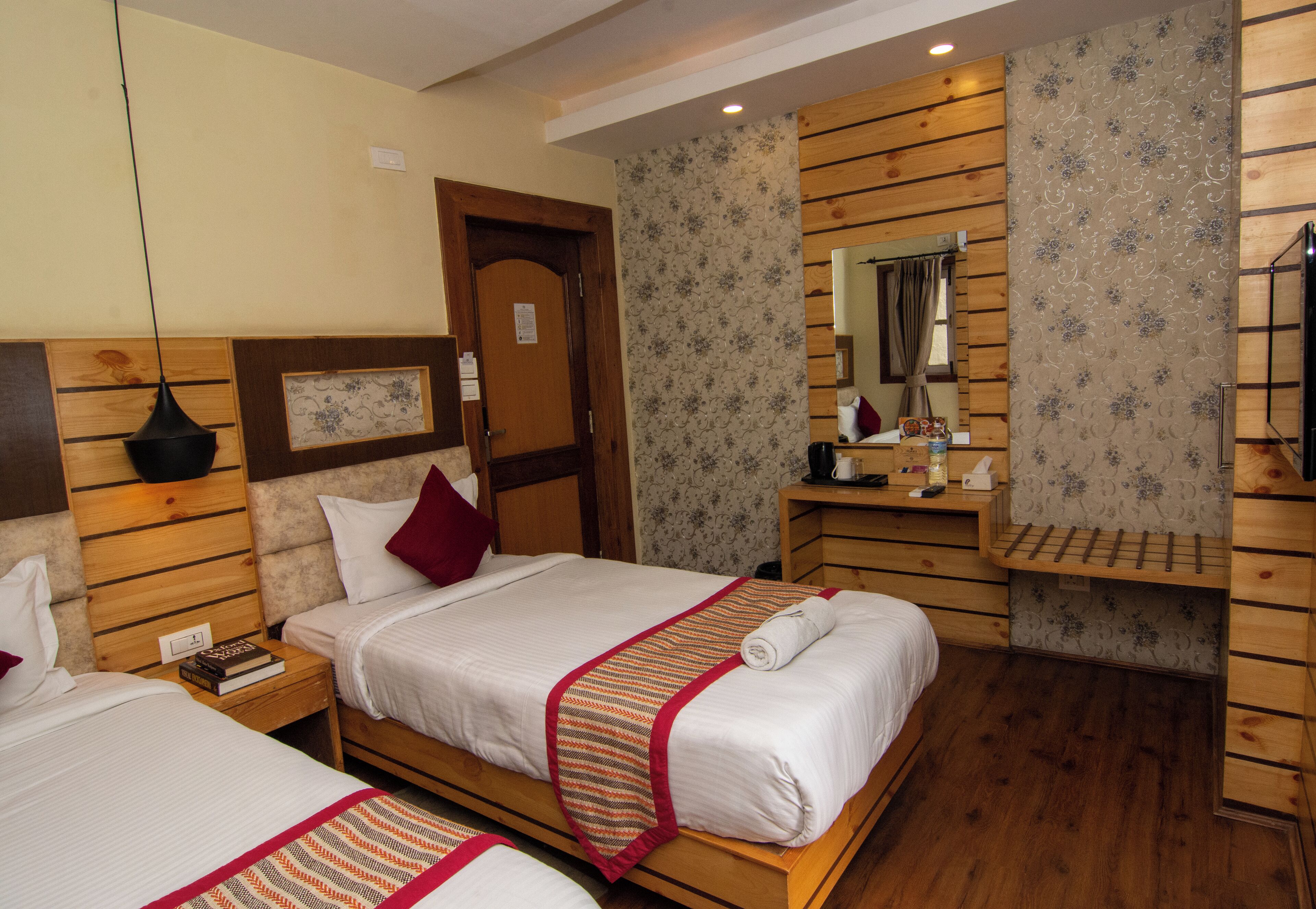 Habitación de hotel con dos camas, cabeceros de madera, un aparador de madera, un espejo y una mesita de noche con una lámpara.