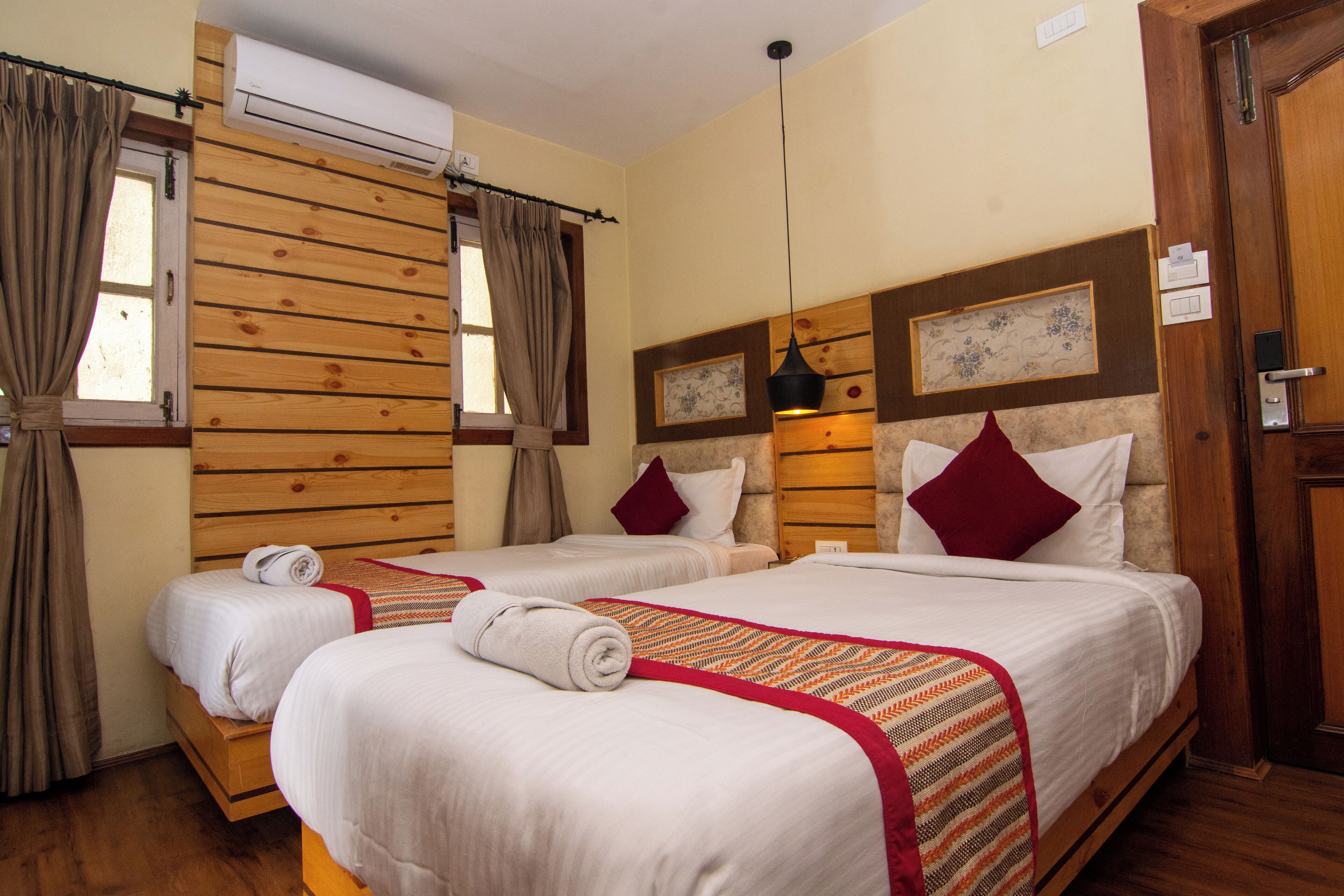 Habitación de hotel con dos camas, paneles de madera, un ventanal con cortinas y un aire acondicionado instalado en la pared.
