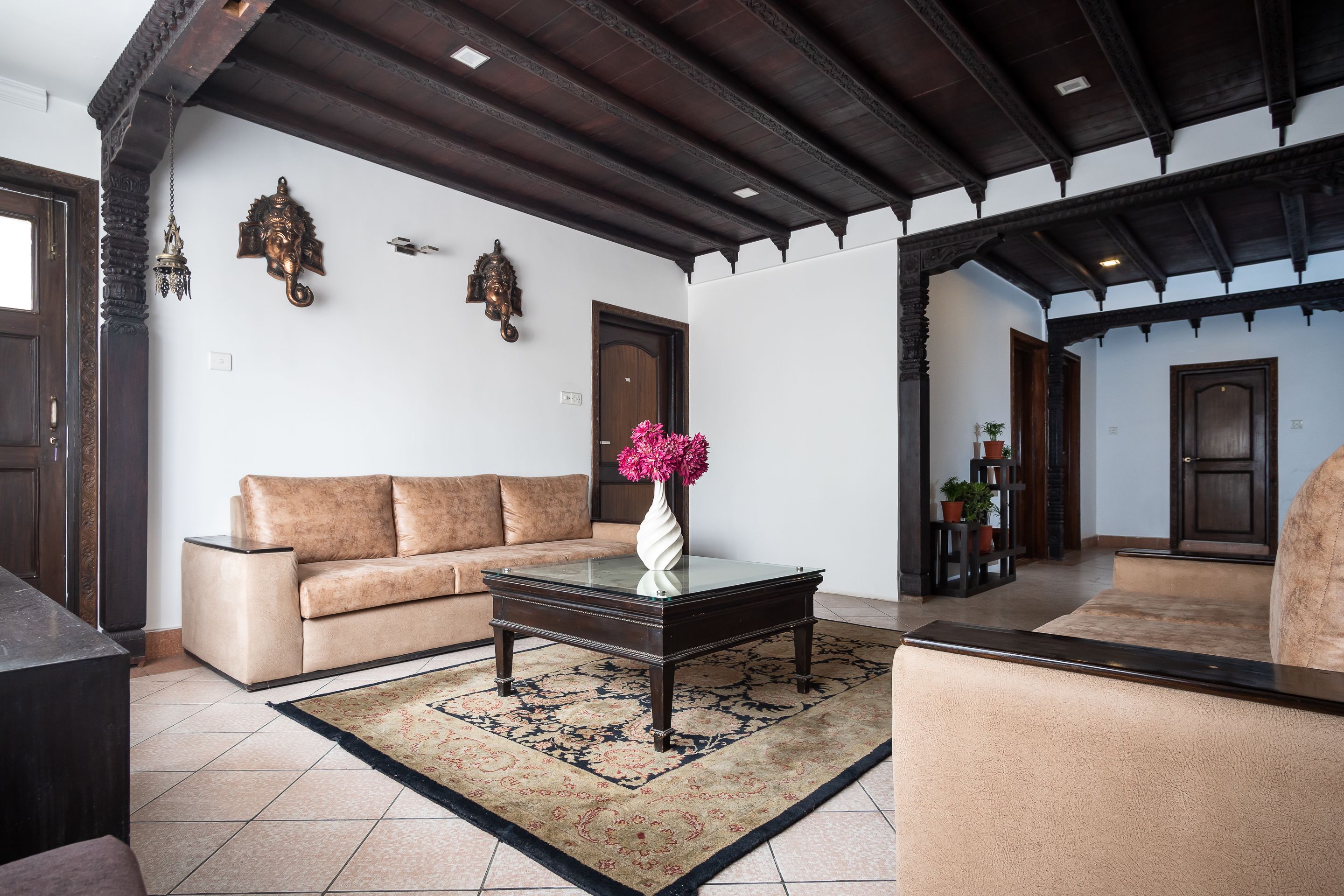 Una sala de estar con sofá, una mesa de centro de vidrio, alfombra estampada y un jarrón decorativo.