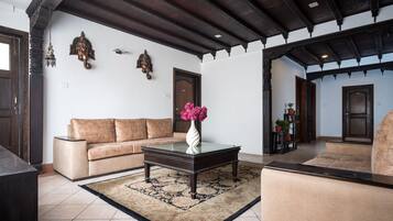 Una sala de estar con sofá, una mesa de centro de vidrio, alfombra estampada y un jarrón decorativo.