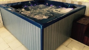 Banheira de hidromassagem com parede de pedra ao fundo e piso revestido.
