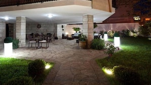 Área de pátio externa com piso de pedra, disposição de assentos e plantas em vasos.