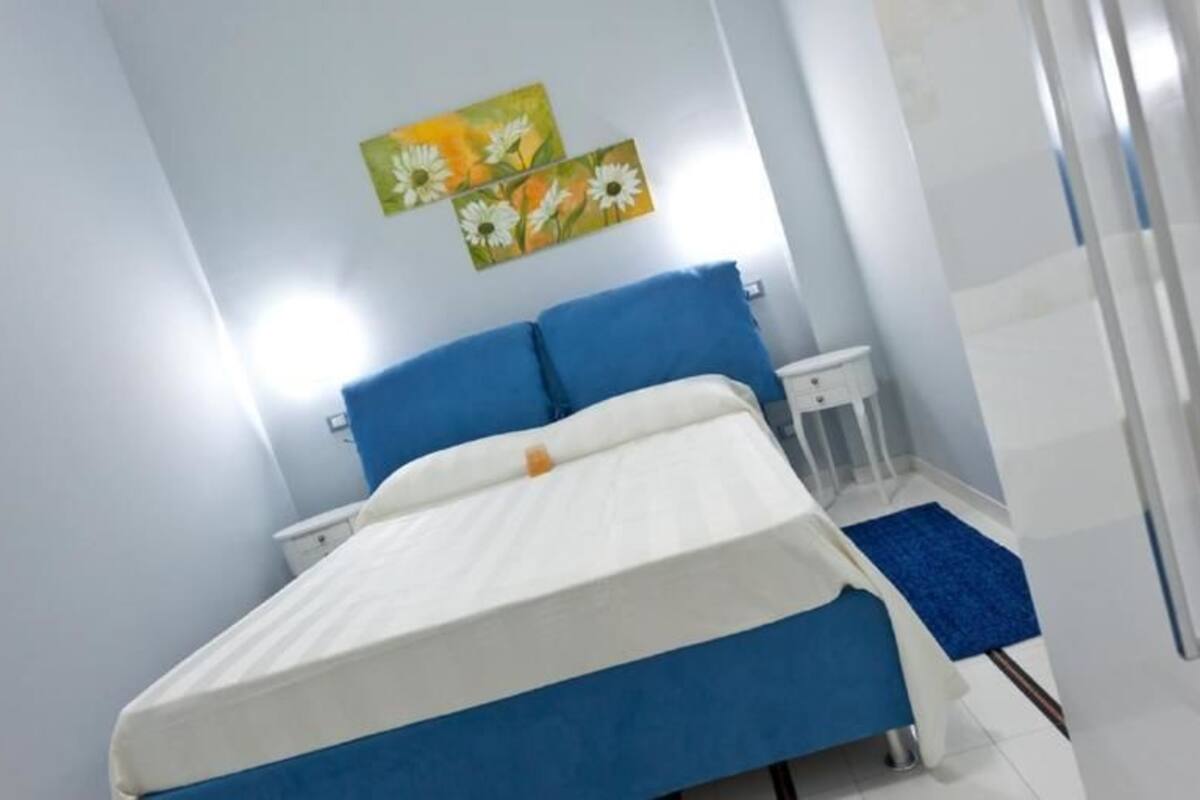 Quarto com cama, mesa de cabeceira, mesinha e uma parede com arte floral.