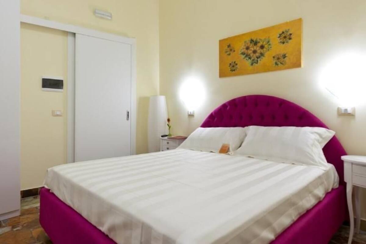 Quarto com cama, guarda-roupa, mesa de cabeceira e luminária na parede.