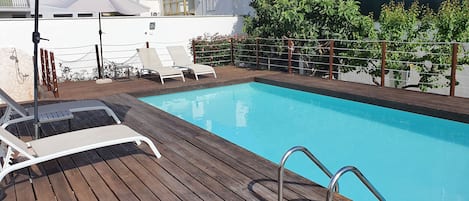 A wooden deck with a swimming pool, lounge chairs, and a covered area with umbrellas.