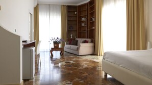 Quarto de hotel com cama, sofá, escrivaninha e estante embutida.
