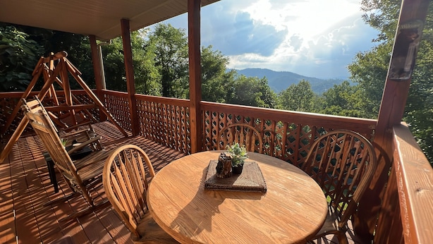 A wooden deck with a round table and chairs, a hanging chair, and a view of mountains and trees. - A piece of Heaven on Earth with all the comforts of home! (Gatlinburg)