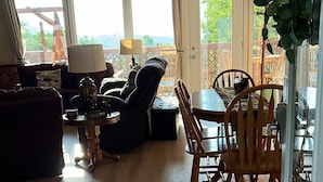 A cozy living room with a sofa, a coffee table, and a dining area with a table and chairs. There is a large window with a view of greenery outside. - A piece of Heaven on Earth with all the comforts of home! (Gatlinburg)