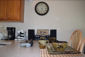 Cozy cabin kitchen with a vintage-style clock, coffee maker, and welcoming sign.