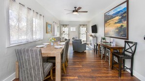 A spacious dining area with a wooden table set for four, flanked by striped chairs. A ceiling fan is visible above, and a large landscape painting adorns the wall. - Historical, Renovated Home In Downtown, Near Pools (Glenwood Springs)