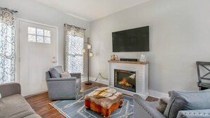 A living room with a fireplace, a flat-screen TV, and two armchairs. - Historical, Renovated Home In Downtown, Near Pools (Glenwood Springs)